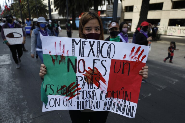 A demonstrator carries a sign reading in Spanish, "Mexico is not a country, it's a mass grave with a national anthem," as people march to protest violence against women on International Women's Day, March 8, 2021, in Mexico City. Women across the world will demand equal pay, reproductive rights, education, justice and other essential needs during demonstrations marking International Women’s Day on Friday, March 8, 2024. (AP Photo/Rebecca Blackwell, File)