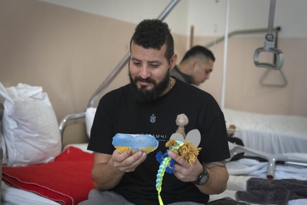 A wounded professional soldier from Medellín, Colombia who goes by the call sign of Checho, 32, smiles as he holds gifts from Ukrainian children in a hospital in Ukraine Wednesday, Dec. 20, 2023. (AP Photo/Efrem Lukatsky)