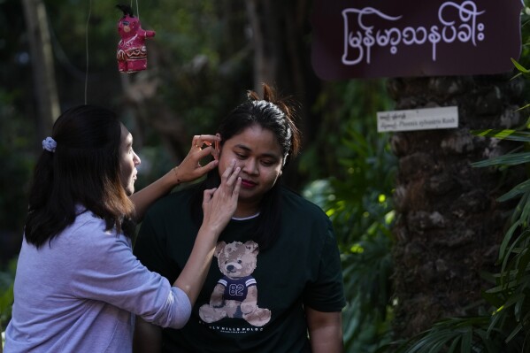A girl helps to put Thanakha, traditional make-up, on face as during performance competition show aiming to submit the traditional culture of Thanakha to UNESCO's Intangible Cultural Heritage of Humanity, Wednesday, Feb.12, 2025 in Yangon, Myanmar. (AP Photo/Thein Zaw)