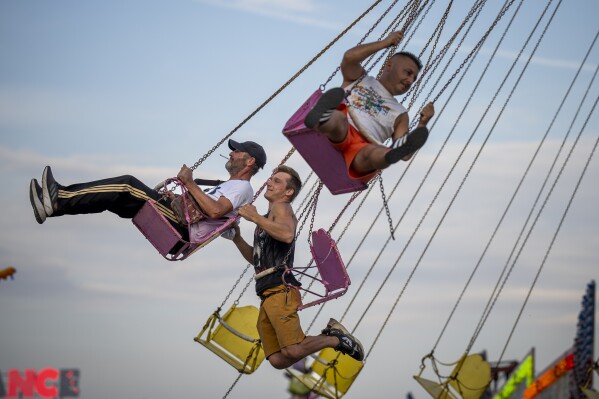 Men enjoy a swing ride at a fair in Hagioaica, Romania, Thursday, Sept. 14, 2023. For many families in poorer areas of the country, Romania's autumn fairs, like the Titu Fair, are one of the very few still affordable entertainment events of the year. (AP Photo/Andreea Alexandru)