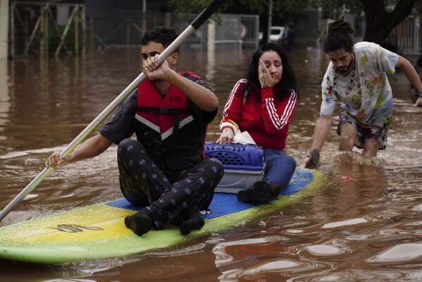 Mensen evacueren op een surfplank uit een wijk die overstroomd is door hevige regen, in Canoas, staat Rio Grande do Sul, Brazilië, zaterdag 4 mei 2024. (AP Photo/Carlos Macedo)