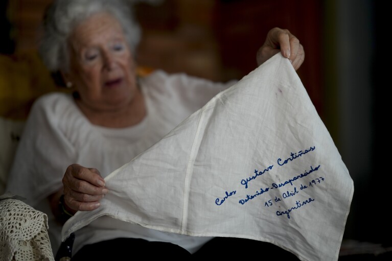Nora Cortinas holds a scarf embroidered with the name of her missing son Gustavo, which she never leaves home without, at her home on the outskirts of Buenos Aires, Argentina, Monday, Jan. 29, 2024. Cortinas became one of many mothers whose children were kidnapped by the state when Gustavo disappeared on April 15, 1977, giving birth to what is today’s human rights organization, the Mothers of Plaza de Mayo. (AP Photo/Natacha Pisarenko)