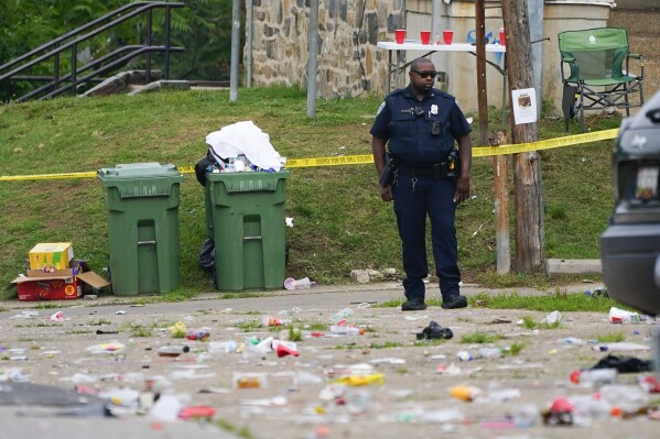 FILE - A police officer stands in the area of a mass shooting incident in the Southern District of Baltimore, Sunday, July 2, 2023. Baltimore leaders are condemning what they called a “catastrophic breakdown” in how city police responded to 911 calls leading up to a mass shooting at a neighborhood block party earlier this month. Police received a call about hundreds of partygoers armed with guns and knives about three hours before the shooting, but on-duty officers decided no law enforcement services were required.(AP Photo/Julio Cortez, File)