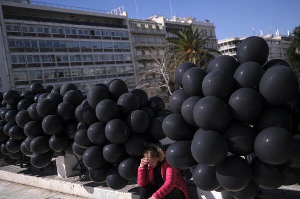 A woman sits among black balloons, during a protest outside the Greek parliament, in Athens, Greece, Sunday, March 5, 2023. Thousands protesters, take part in rallies around the country for fifth day, protesting the conditions that led the deaths of dozens of people late Tuesday, in Greece's worst recorded rail accident. (AP Photo/Aggelos Barai)