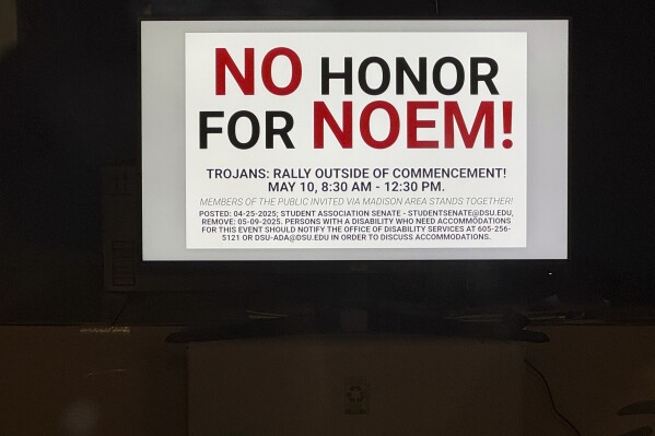 A banner on a television monitor in the student senate office is displayed in Dakota State University's Trojan Center, calling for students to protest Homeland Security Secretary Kristi Noem's commencement speech, Monday, April 28, 2025, in Madison, S.D. (AP Photo/Sarah Raza)