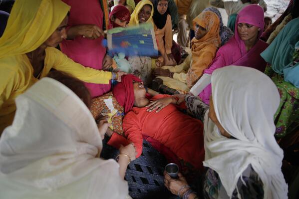 In this Tuesday, July 24, 2018 photo, Asmina Bano, wife of Rakbar Khan, is comforted by family members and neighbors as she lies on a cot outside her home in Kolgaon village, India. Khan, a cattle trader, died after being thrashed by a mob last week on suspicion of cattle smuggling. A series of mob attacks on minority groups involved in cattle trade have occurred since the Hindu nationalist Bharatiya Janata Party swept elections in 2014. Cows are considered sacred in Hindu-majority India, and slaughtering them or eating beef is illegal or restricted across much of the country. (AP Photo/Altaf Qadri)