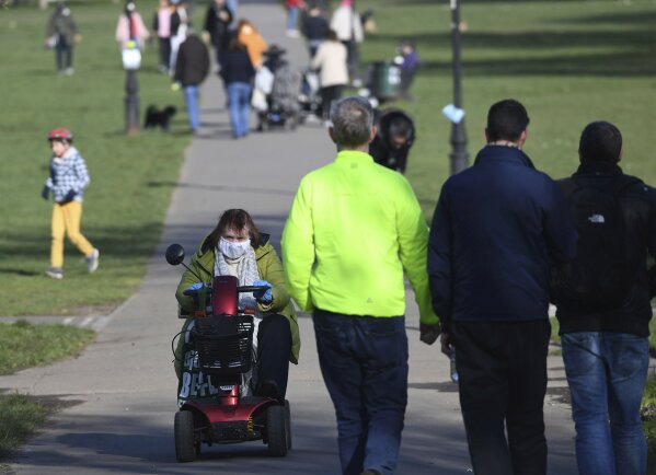 A woman on a mobility scooters passes pedestrians using a path across Clapham Common in south London, Monday March 23, 2020. The British government is warning that it may introduce more draconian measures to slow the coronavirus if people persist in ignoring social distancing recommendations. (Stefan Rousseau/PA via AP)
