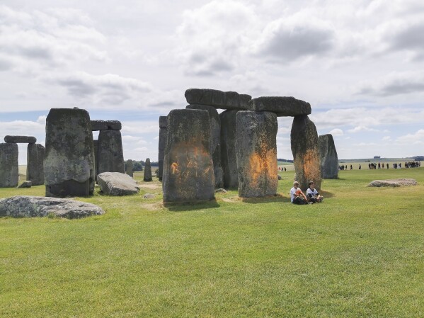 In this handout photo, Just Stop Oil protesters sit after spraying an orange substance on Stonehenge, in Salisbury, England, Wednesday June 19, 2024. (Just Stop Oil via AP)