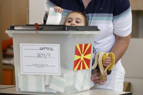 A girl casts the ballot of an adult during the parliamentary election and the presidential runoff, at a polling station in Skopje, North Macedonia, on Wednesday, May 8, 2024. Voters in North Macedonia go to the polls Wednesday for a double election — parliamentary and presidential — following a campaign in which the country's aspirations to join the European Union have played a central role. (AP Photo/Boris Grdanoski)