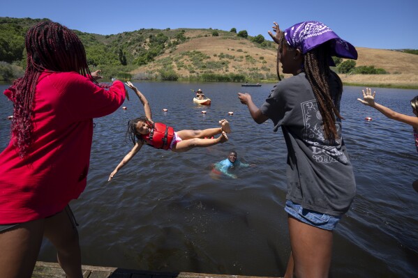 Maya Johnson, 7, of New York, is playfully swung into the lake by her friends during Camp Be'chol Lashon, a sleepaway camp for Jewish children of color, Friday, July 28, 2023, in Petaluma, Calif., at Walker Creek Ranch. (AP Photo/Jacquelyn Martin)