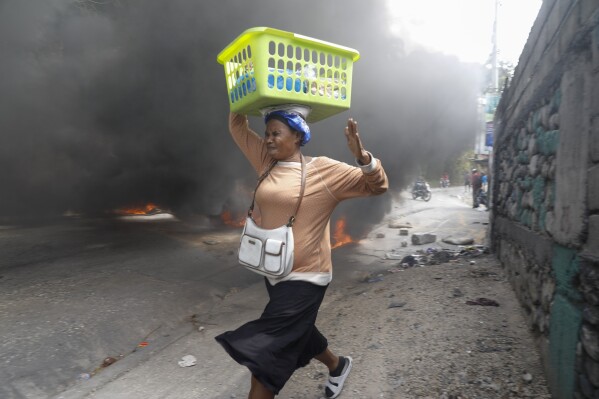 Una mujer pasa corriendo junto a una barricada de neumáticos en llamas colocada por manifestantes contrarios al primer ministro, Ariel Henry, en Puerto Príncipe, Haití, el 5 de febrero de 2024. (AP Foto/Odelyn Joseph)