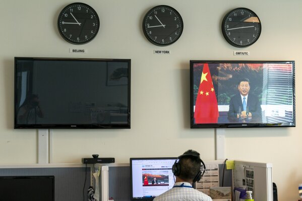 A reporter with the Xinhua Press Agency watches as President Xi Jinping is seen on a video screen remotely addressing the 75th session of the United Nations General Assembly, Tuesday, Sept. 22, 2020, at U.N. headquarters. This year's annual gathering of world leaders at U.N. headquarters will be almost entirely "virtual." Leaders have been asked to pre-record their speeches, which will be shown in the General Assembly chamber, where each of the 193 U.N. member nations are allowed to have one diplomat present. (AP Photo/Mary Altaffer)
