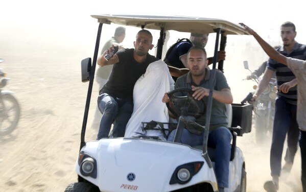 Palestinians transport a captured Israeli civilian from Kibbutz Kfar Azza into the Gaza Strip on Saturday, Oct. 7, 2023. The militant Hamas rulers of the Gaza Strip carried out an unprecedented, multi-front attack on Israel at daybreak Saturday, firing thousands of rockets as dozens of Hamas fighters infiltrated the heavily fortified border in several locations by air, land, and sea and catching the country off-guard on a major holiday. (AP Photo/Hatem Ali)