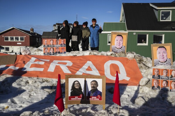 Children stand in the snow as candidate's pictures on boards are seen outside a polling station during parliamentary elections, in Nuuk, Greenland, March 11, 2025. (AP Photo/Evgeniy Maloletka)