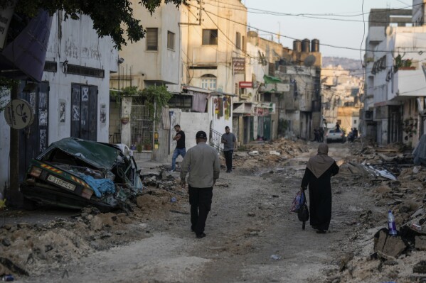 Palestinians walk on a damaged road following two days of Israeli military raid on the militant stronghold of the Jenin refugee camp in the West Bank, Wednesday, July 5, 2023. The Israeli military says it has withdrawn its troops from the refugee camp. The pullout Wednesday morning ended an intense two-day operation that killed at least 13 Palestinians, drove thousands of people from their homes and left a wide swath of damage in its wake. One Israeli soldier was also killed. (AP Photo/Majdi Mohammed)