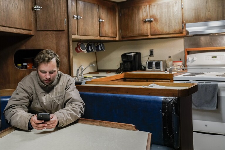 Sam Stern checks his phone while relaxing inside the a fishing boat's galley, Monday, June 26, 2023, in Kodiak, Alaska. (AP Photo/Joshua A. Bickel)