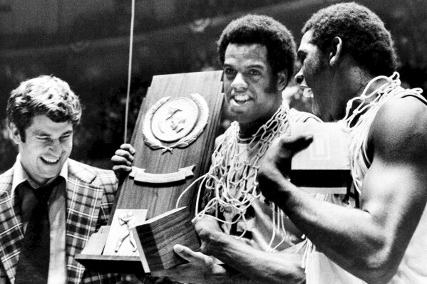 FILE - Indiana coach Bobby Knight, left, and team members Scott May, center, and Quinn Buckner, right, celebrate with the trophy after winning the NCAA college basketball championship, beating Michigan 86-68 in Philadelphia, March 30, 1976. (AP Photo/File)