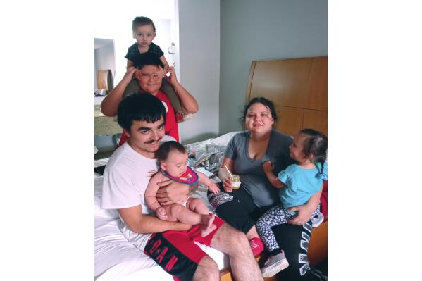 In this photo provided by Shelly Savoie, Timothy Auxilien and Ressa Savoie sit in a hotel room with their 6-month-old daughter, August, and Ressa's siblings, Julian and twins Summer and Winter, in Bossier City, La., on Monday, Aug. 30, 2021. The family is staying in Bossier City after evacuating from their home in Jefferson Parish, La., on Saturday to escape Hurricane Ida. Ressa's mother, Shelly, said they were able to pay for a hotel room for a few nights after their home was damaged during the storm, but said they don’t have money to stay longer. (Shelly Savoie via AP)