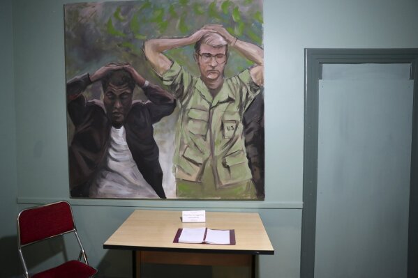 In this Sept. 26, 2019, photo, a painting of one of the images of the takeover of U.S. Embassy in Tehran in 1979 which shows U.S. Marine Sgt. Ladell Maples of Earle, Ark., left, and Cpl. Steve Kirtley of Little Rock, Ark., with their hands above their heads adorns a wall of the embassy, now partly a museum, in Tehran, Iran.  Images like those of surrendering American troops carry a strong resonance for hard-liners in Iran. (AP Photo/Vahid Salemi)