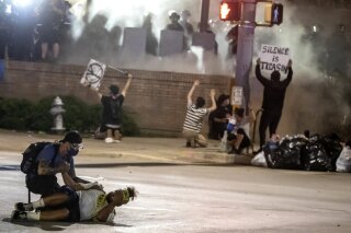 FILE - In this May 30, 2020 file photo, people help a protester after he was shot with a rubber bullet under Interstate 35 freeway in Austin Texas while protesting the death of George Floyd. A group of doctors in Austin is warning police not to use so-called “less lethal” munitions for crowd control after they treated people who were severely hurt during protests in May. In a letter published Friday, Aug. 14, in the New England Journal of Medicine, 12 doctors from the Dell Seton Medical Center at The University of Texas say Austin police who fired bean bag rounds caused injuries including bleeding on the brain and a skull fracture. (Ricardo B. Brazziell/Austin American-Statesman via AP, File)
