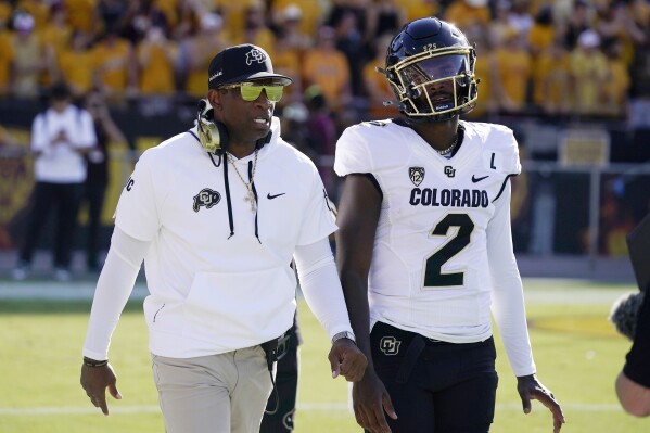 FILE - Colorado head coach Deion Sanders, left, talks with his son and starting quarterback Shedeur Sanders (2) prior to an NCAA college football game against Arizona State, Saturday, Oct. 7, 2023, in Tempe, Ariz. Colorado coach Deion Sanders said the fracture in the back of his quarterback son, Shedeur, has healed and he's gearing up for the spring game on April 27, 2024. Shedeur Sanders missed the final game last season due to the fracture. (AP Photo/Ross D. Franklin, File)