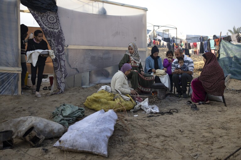 Members of the Abu Jarad family, who were displaced by the Israeli bombardment of the Gaza Strip, bake bread at a makeshift tent camp in the Muwasi area, southern Gaza, Monday, Jan. 1, 2024. (AP Photo/Fatima Shbair)