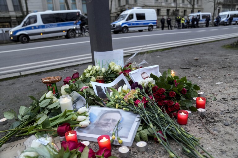 Portraits of jailed Russian opposition leader Alexei Navalny, flowers and candles are laid on a ground as police guard and people protest in front of the Russian embassy in Berlin, Germany, Friday, Feb. 16, 2024. (AP Photo/Ebrahim Noroozi)