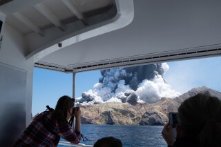 FILE - In photo provided by Michael Schade, tourists on a boat look at the eruption of the volcano on White Island, New Zealand, Dec. 9, 2019. Tour booking agents and managers of a New Zealand island where a volcanic eruption killed 22 people in 2019 were ordered Friday, March 1, 2024 to pay nearly $13 million (US$7.8 million) in fines and reparations. (Michael Schade via AP, File)