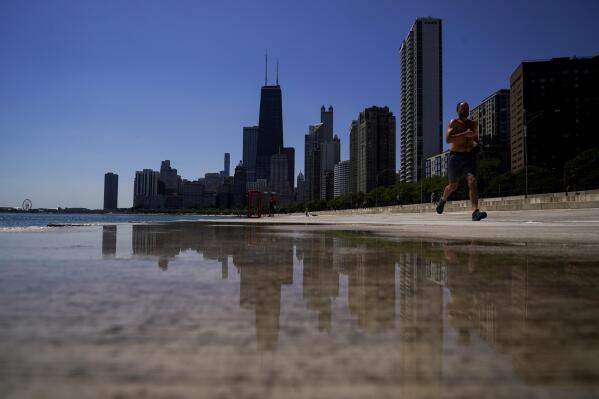 A runner jogs along the shore of Lake Michigan Wednesday, July 20, 2022, as downtown Chicago skyline is seen in the background. (AP Photo/Kiichiro Sato)