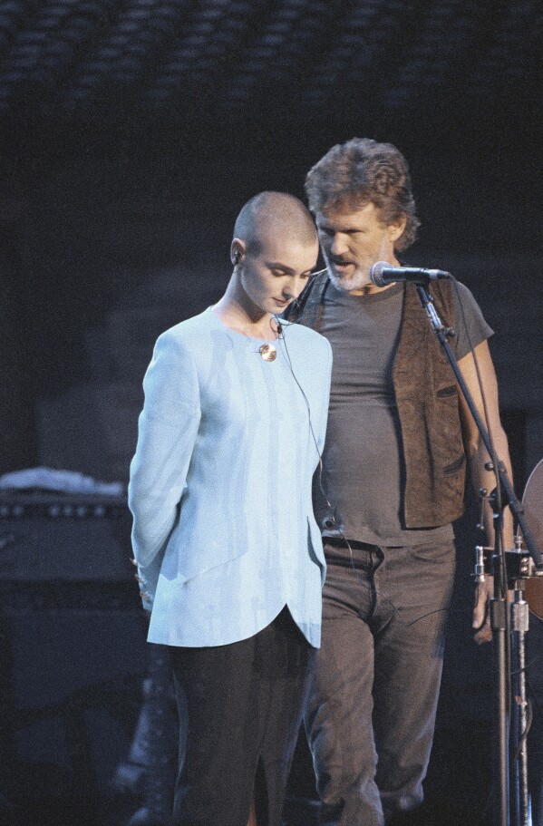 FILE - Kris Kristofferson comforts Sinead O'Connor after she was booed off stage during the Bob Dylan anniversary concert at New York Madison Square Garden, on Oct. 17, 1992. The performance was O'Connor's first live event since she ripped a picture of Pope John Paul II during a performance on "Saturday Night Live." O’Connor, the gifted Irish singer-songwriter who became a superstar in her mid-20s but was known as much for her private struggles and provocative actions as for her fierce and expressive music, has died at 56. The singer's family issued a statement reported Wednesday by the BBC and RTE. (AP Photo/Ron Frehm, File)