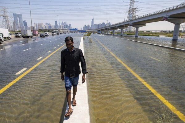 A man walks along a road barrier among floodwater caused by heavy rain on Sheikh Zayed Road highway in Dubai, United Arab Emirates, Thursday, April 18, 2024. The United Arab Emirates attempted to dry out Thursday from the heaviest rain the desert nation has ever recorded, a deluge that flooded out Dubai International Airport and disrupted flights through the world's busiest airfield for international travel. (AP Photo/Christopher Pike)