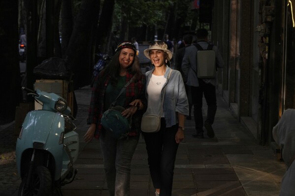 Two women share a laugh as they walk on the sidewalk in northern Tehran, Iran, Saturday, May 3, 2025. (AP Photo/Vahid Salemi)