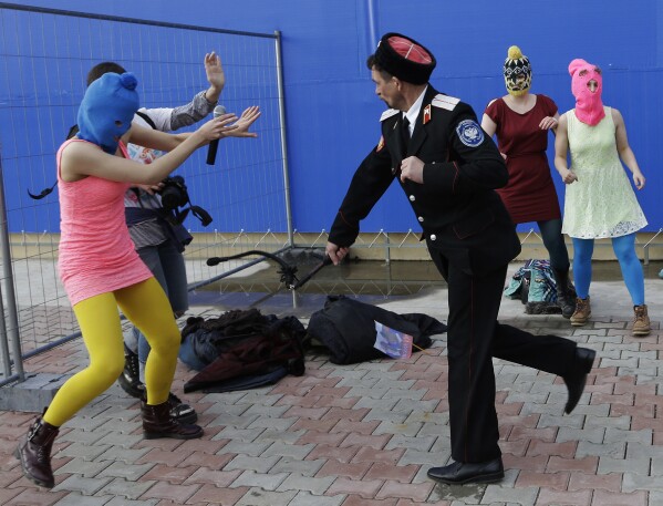 FILE - A Cossack militiaman attacks Nadezhda Tolokonnikova, left, and a photographer as she and fellow members of the punk group Pussy Riot, including Maria Alekhina, right, in the pink balaclava, stage a protest in Sochi, Russia, on Wednesday, Feb. 19, 2014. While the Sochi Olympics were under way, members of the hard-line Russian nationalist militia beat and whipped the protesters who demonstrated in Sochi. (AP Photo/Morry Gash, File)