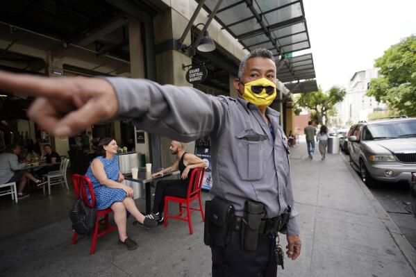 A private security guard points to the street site near Grand Central Market, Sunday, May 15, 2022, in Los Angeles. Police are searching for a suspect in the fatal shooting of a man outside the popular food hall. (AP Photo/Damian Dovarganes)