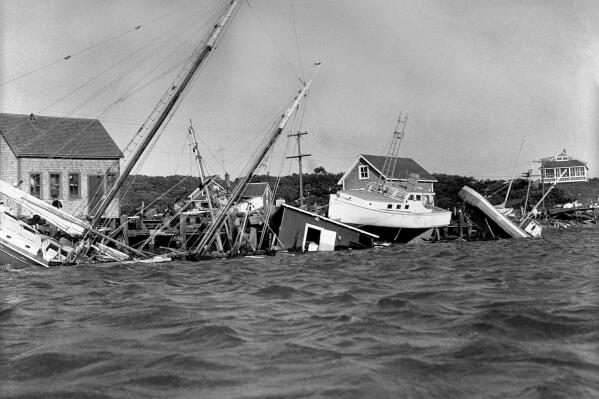 FILE - This Aug. 31, 1954 file photo shows boats driven up onto docks and buildings, and knocked into the water in the Menemsha section of Martha's Vineyard as a howling Hurricane Carol accompanied by fiercely driving rain struck New England causing millions of dollars of damage. An environmental report being released Wednesday, Aug. 4, 2021 paints a dire picture for the famous islands of Martha's Vineyard and Nantucket in Massachusetts in the face of rising sea levels and more powerful coastal storms caused by climate change. (AP Photo/DCG, File)