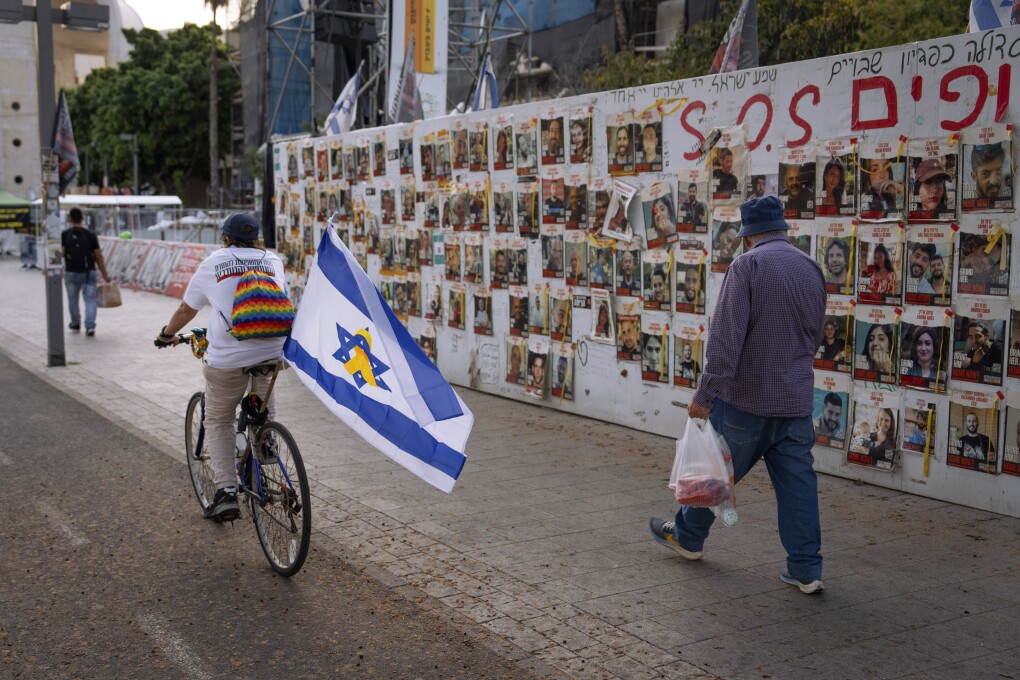 Passersby observe the photos of hostages held in the Gaza Strip that are plastered to the walls of a plaza known as Hostages Square in Tel Aviv, Israel, Friday, May 17, 2024. (AP Photo/Oded Balilty).