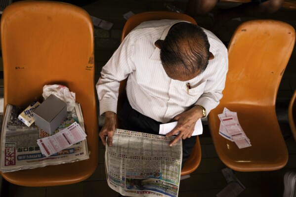 A visitor reads a horse racing paper at the Macao Jockey Club in Macao, Saturday, March 30, 2024. After more than 40 years, Macao’s horse racing track hosted its final races on Saturday, bringing an end to the sport in the city famous for its massive casinos. (AP Photo/Louise Delmotte)