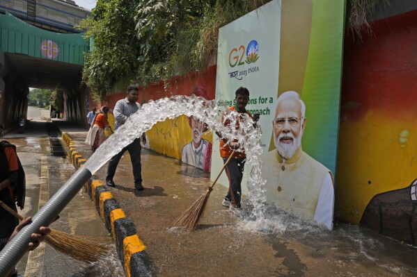 Municipal workers wash a side walk near a billboard featuring Indian Prime Minister Narendra Modi ahead of this week's summit of the Group of 20 nations, in New Delhi, India, Thursday, Sept. 7, 2023. (AP Photo/Manish Swarup)