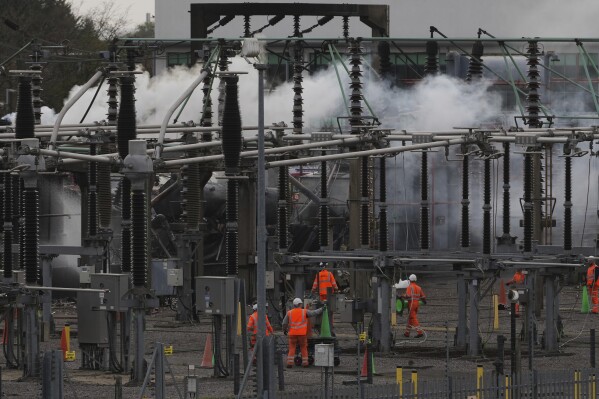 Workers are seen as smoke rises from the North Hyde electrical substation, which caught fire last night, leading to the closure of the Heathrow Airport, in London, Friday March 21, 2025.(AP Photo/Kirsty Wigglesworth)