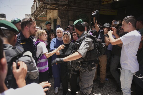 Israeli police officers escort Palestinian women while Israelis marking Jerusalem Day, an Israeli holiday celebrating the capture of east Jerusalem in the 1967 Mideast war, in Jerusalem's Old City, Monday, May 26, 2025. (AP Photo/Ohad Zwigenberg)