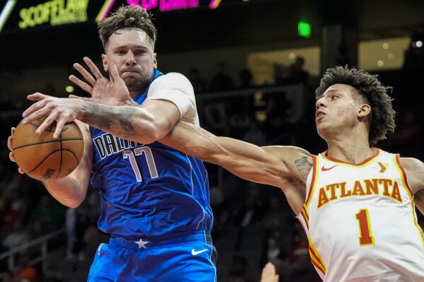 Dallas Mavericks guard Luka Doncic (77) grabs a rebopund from Atlanta Hawks forward Jalen Johnson (1) during the first half of an NBA basketball game, Friday, Jan. 26, 2024, in Atlanta. (AP Photo/Mike Stewart)