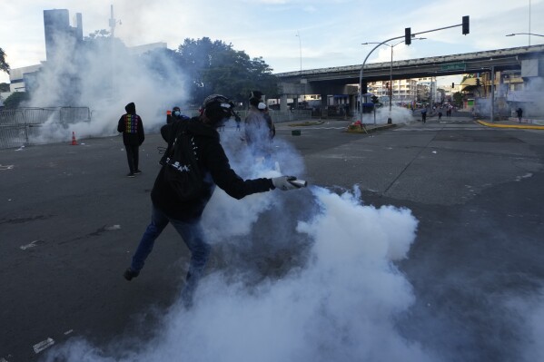 A demonstrator throws back a tear gas canister during clashes with the police at a protest against a recently approved mining contract between the government and Canadian mining company First Quantum, outside the National Assembly in Panama City, Monday, Oct. 23, 2023. (AP Photo/Arnulfo Franco)