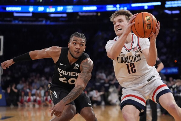 UConn's Cam Spencer (12) protects the ball from Xavier's Dayvion McKnight (20) during the first half of an NCAA college basketball game in the quarterfinal round of the Big East Conference tournament, Thursday, March 14, 2024, in New York. (AP Photo/Frank Franklin II)