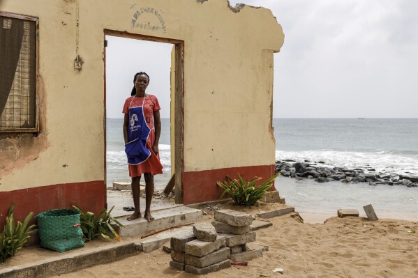 Makafui Atayi stands at the entrance of the remains of her father's 10-unit family home in Avegadzi, Ghana, Tuesday, March 4, 2025 (AP Photo/Misper Apawu)