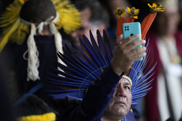 An Indigenous representative takes a photo as he waits for the start of the closing ceremony of the 1st Ordinary Meeting of the National Council for Indigenous Policy, in Brasilia, Brazil, April 18, 2024. (AP Photo/Eraldo Peres)