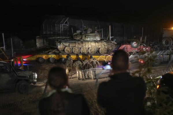 An Israeli truck carries a Syrian tank from the buffer zone near the so-called Alpha Line that separates the Israeli-controlled Golan Heights from Syria, viewed from the town of Majdal Shams, Dec. 21, 2024. (AP Photo/Matias Delacroix, File)