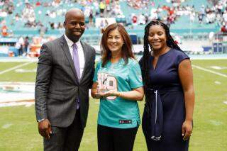 FILE - Maria C. Alonzo, center, as part of the NFL's Hispanic Heritage Leaderships Awards is joined by Miami Dolphins senior vice president Jason Jenkins, left, during the first half at an NFL football game, Sunday, Sept. 15, 2019, in Miami Gardens, Fla.  The woman to the right is unidentified. Jason Jenkins, who spent 13 years with the Miami Dolphins and eventually became the team's senior vice president of communications, died unexpectedly Saturday, Aug. 27, 2022, the team said. (AP Photo/Wilfredo Lee, File)