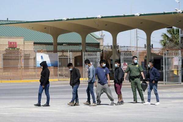 Migrants who were caught trying to sneak into the United States are led by a U.S. Customs and Border Protection agent, second from right, at the McAllen-Hidalgo International Bridge while being deported to Reynosa, Mexico, Thursday, March 18, 2021, in Hidalgo, Texas. A surge of migrants on the Southwest border has the Biden administration on the defensive. The head of Homeland Security acknowledged the severity of the problem Tuesday but insisted it's under control and said he won't revive a Trump-era practice of immediately expelling teens and children. (AP Photo/Julio Cortez)