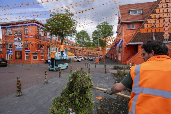 A municipal worker cleans up as orange tarp, orange bunting, and Dutch national flags decorate Marktweg street in The Hague, Netherlands, Thursday June 13, 2024, one day ahead of the start of the Euro 2024 Soccer Championship. The Marktweg is one of several streets in the Netherlands that get an all-encompassing orange facelift during European Championships and World Cups when the national team, known as Oranje after the Dutch royal family and the color of their shirts, are playing. (AP Photo/Peter Dejong)