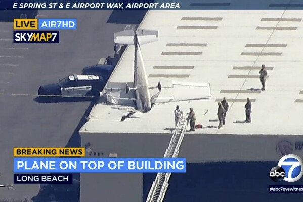 This image taken from video and provided by KABC-7 TV shows a single-engine plane crashed nose-first into the roof of a hangar at Long Beach Airport in Southern California on Monday, July 10, 2023. Authorities say the pilot escaped with only minor injuries. The Federal Aviation Administration said the crash happened while the pilot of the Cessna 172 was practicing landings and takeoffs. (KABC-7 via AP)